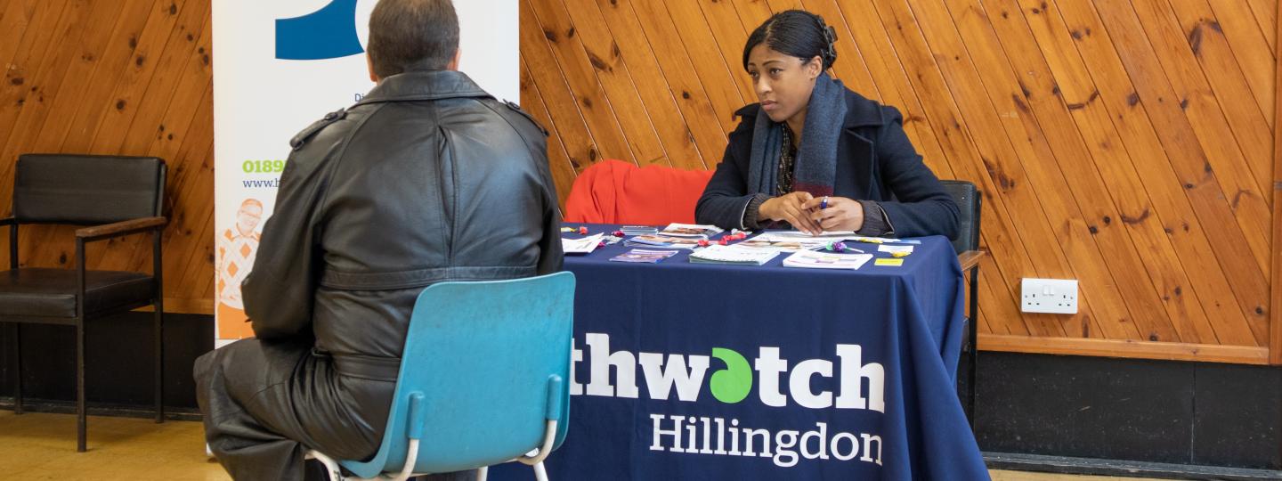 Healthwatch Hillingdon volunteer holding a stall at an event and talking to a member of the public
